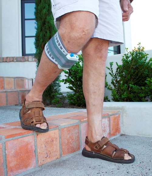 A man wearing a WalkAide medical device on his right leg as he walks down stairs